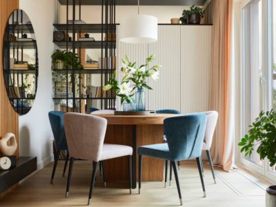 Stylish composition of elegant dining room interior design with velvet armchairs, design rounded wooden table and beautiful personal accessories. Glamour interior design inspiration. Template.