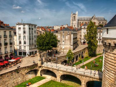 Nantes, France - August 20, 2011: The main entrance of Castle of Brittany Duke's. Many tourists and some banners on the bridge. many people sitting on tables of restaurant  and St. Peter Cathedral on background